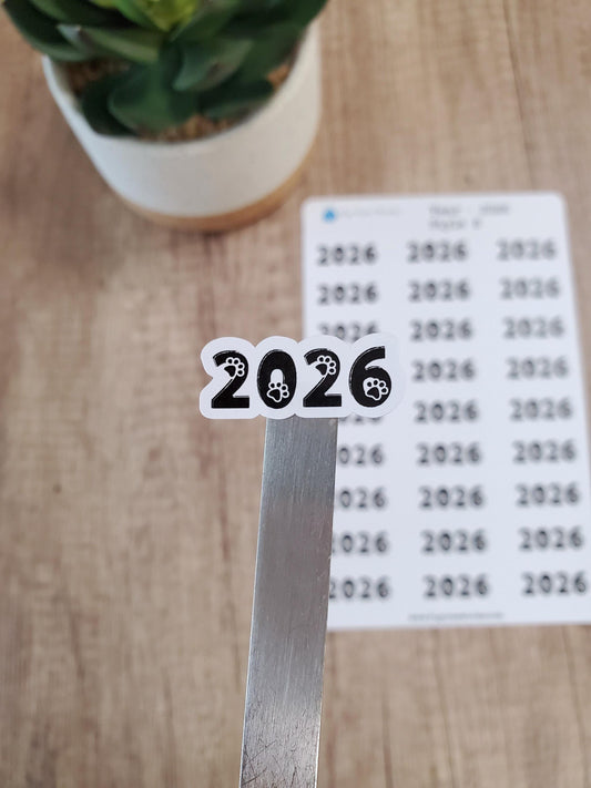 May include: A white sticker with black text and paw prints that reads "2026".